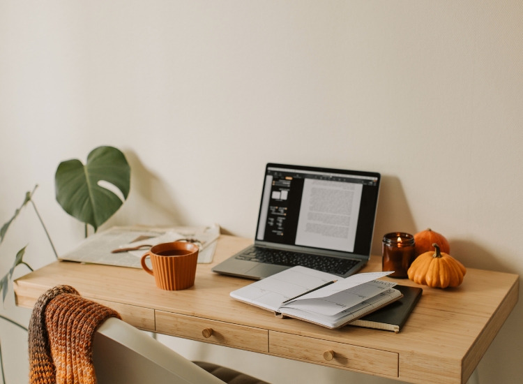 Prijatan radni prostor sa laptopom, planerom, šoljom kafe i sezonskim dekoracijama na drvenom stolu, u toplom i organizovanom okruženju.