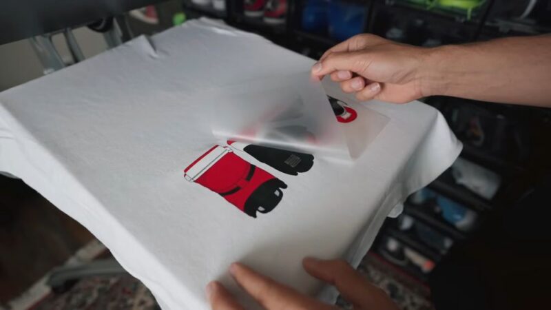 Ruke skidaju foliju sa štampe na beloj majici sa crveno crnim motivom