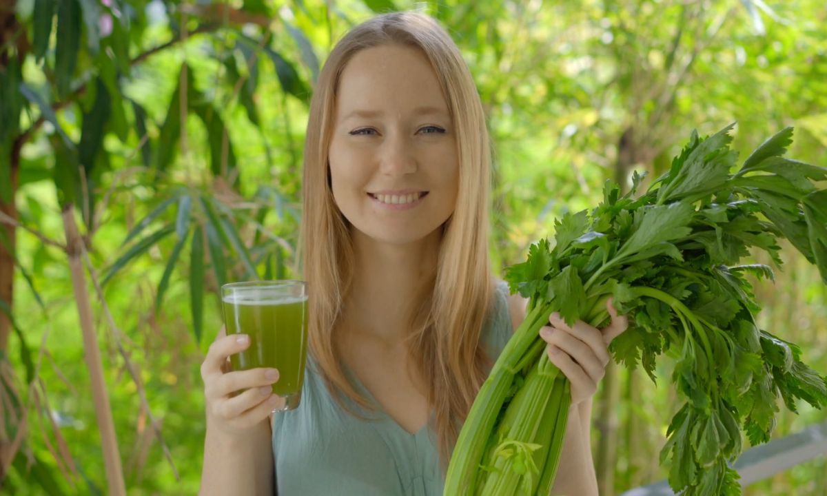 devojka pije sok od celera i drži celer u ruci