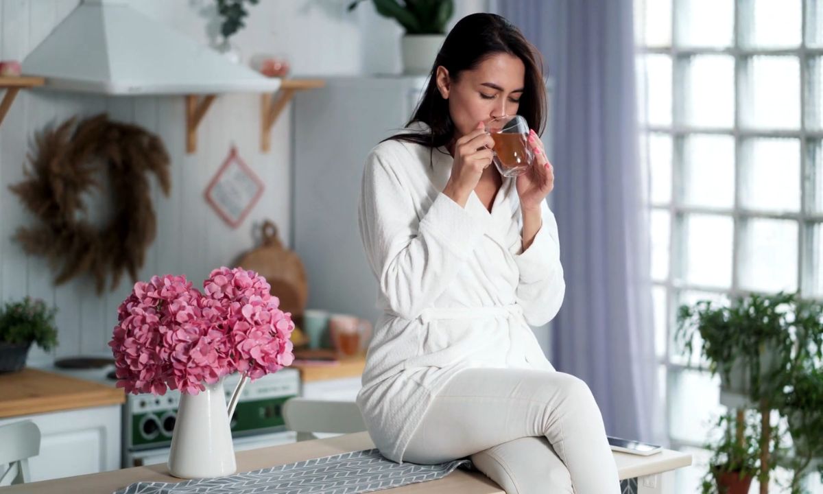 devojka sedi na radnoj površini u kuhinji i pije zeleni čaj