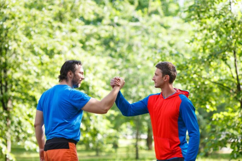 Dva muškarca u sportskoj odeći pozdravljaju se nakon vežbanja u zelenom parku.